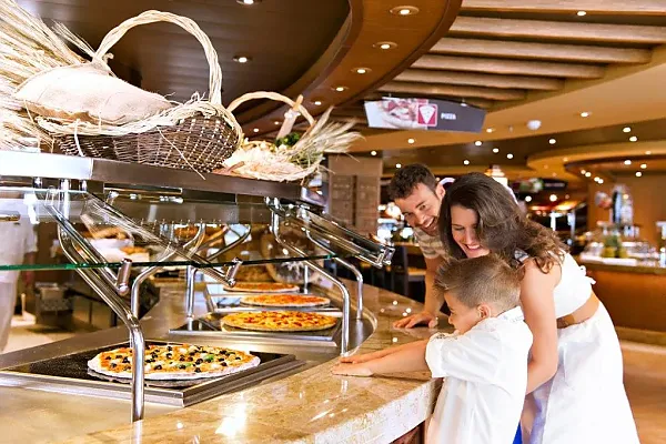 Das Bild zeigt eine Szene in einem Buffet-Restaurant, bei der eine Familie – bestehend aus einem Mann, einer Frau und einem Kind – die Speisen an einer Selbstbedienungstheke betrachtet.