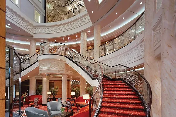 Das Bild zeigt das luxuriöse Atrium und die geschwungene Treppe an Bord des bekannten Ozeandampfers Queen Mary 2.