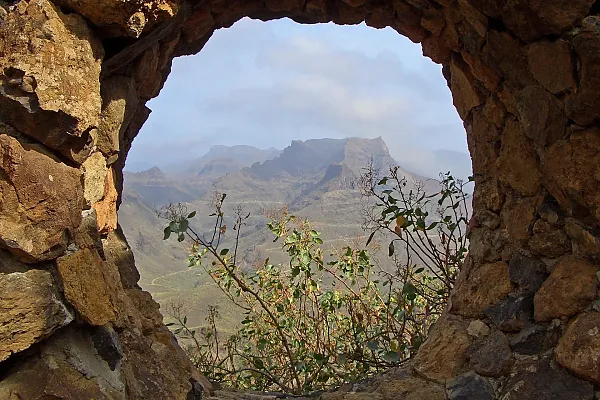 Das Bild zeigt einen Blick durch ein steinernes Fenster auf die bergige Landschaft im Inneren der Insel Gran Canaria.