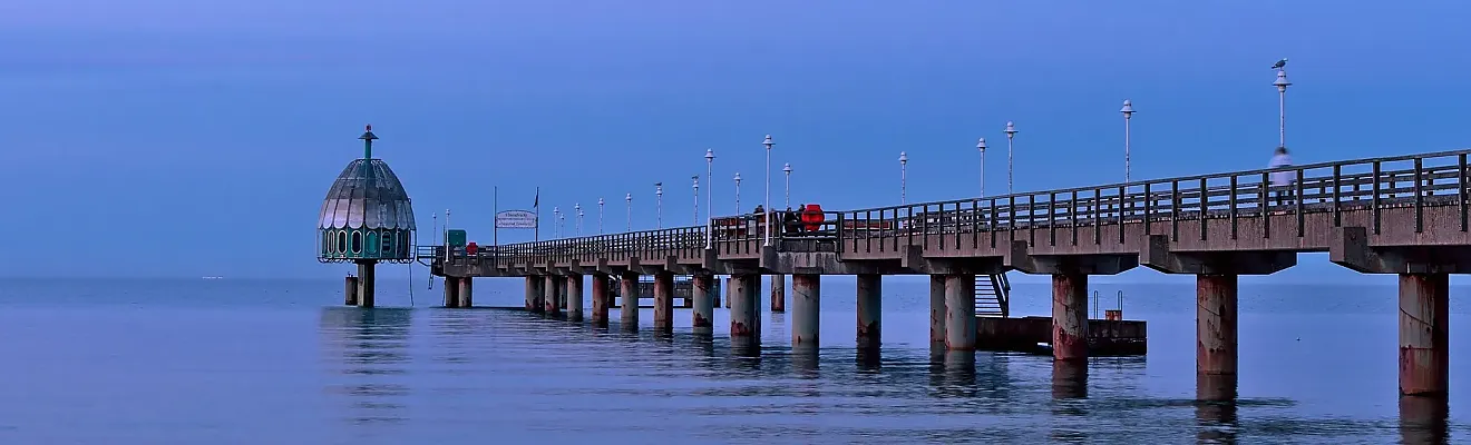 Das Bild zeigt die Seebrücke im Ostseebad Zinnowitz auf der Insel Usedom. Das markante, kuppelförmige Gebäude am Ende der Brücke ist die Tauchgondel Zinnowitz. Diese weltweit einzigartige Attraktion wurde im Jahr 2006 in Betrieb genommen.