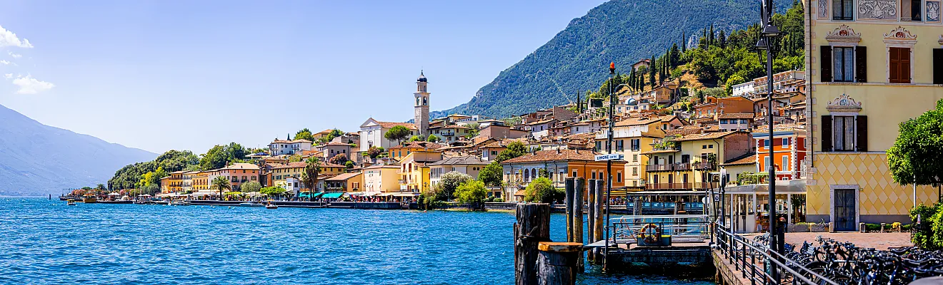 Luftaufnahme von Limone sul Garda, einem farbenfrohen Städtchen am Seeufer in Italien, eingebettet zwischen dem Gardasee und steilen Bergen unter strahlend blauem Himmel