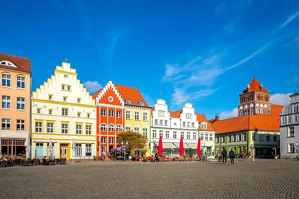 Das Bild zeigt den historischen Marktplatz der Hansestadt Greifswald in Mecklenburg-Vorpommern. Der Platz ist von imposanten Giebelhäusern und Backsteinbauten umgeben.