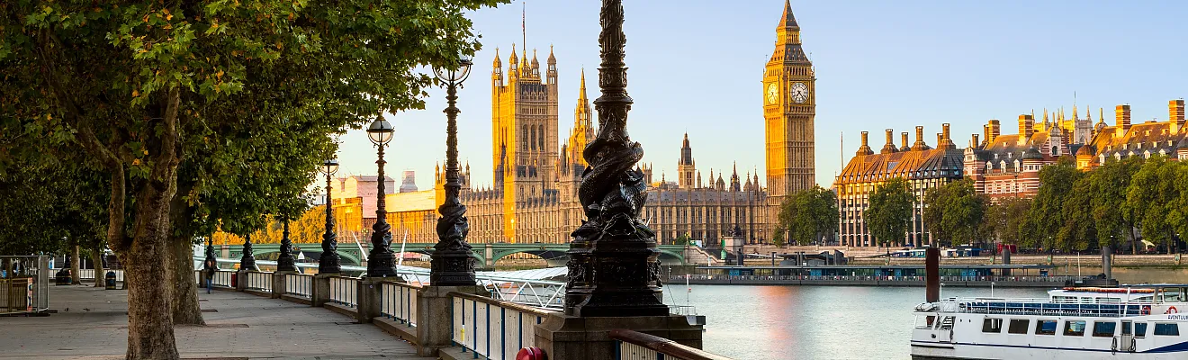Das Bild zeigt einen Moment in London, der die berühmten Wahrzeichen entlang der Themse einfängt. Im Hintergrund ist der britische Parlamentssitz (Palace of Westminster) und der ikonische Glockenturm (Big Ben) zu sehen.