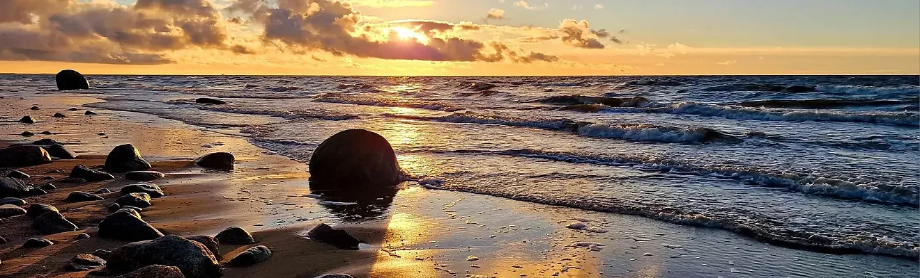 Das Bild zeigt einen stimmungsvollen Sonnenuntergang am Meer mit charakteristische Felsbrocken am Ufer, die typisch für Küstenabschnitte an der Ostsee sind.