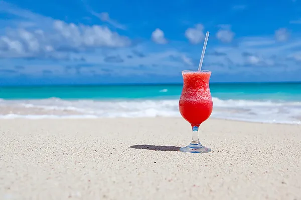 Das Bild zeigt einen erfrischenden roten, gefrorenen Cocktail in einem klassischen Hurricaneglas, der an einem sonnigen Strand serviert wird